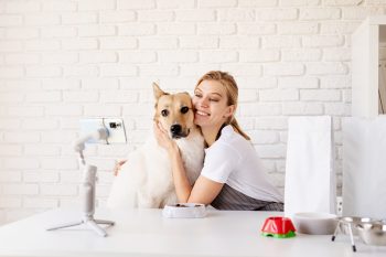 Young caucasian woman groomer blogger speaking looking to camera, having stream with her dog